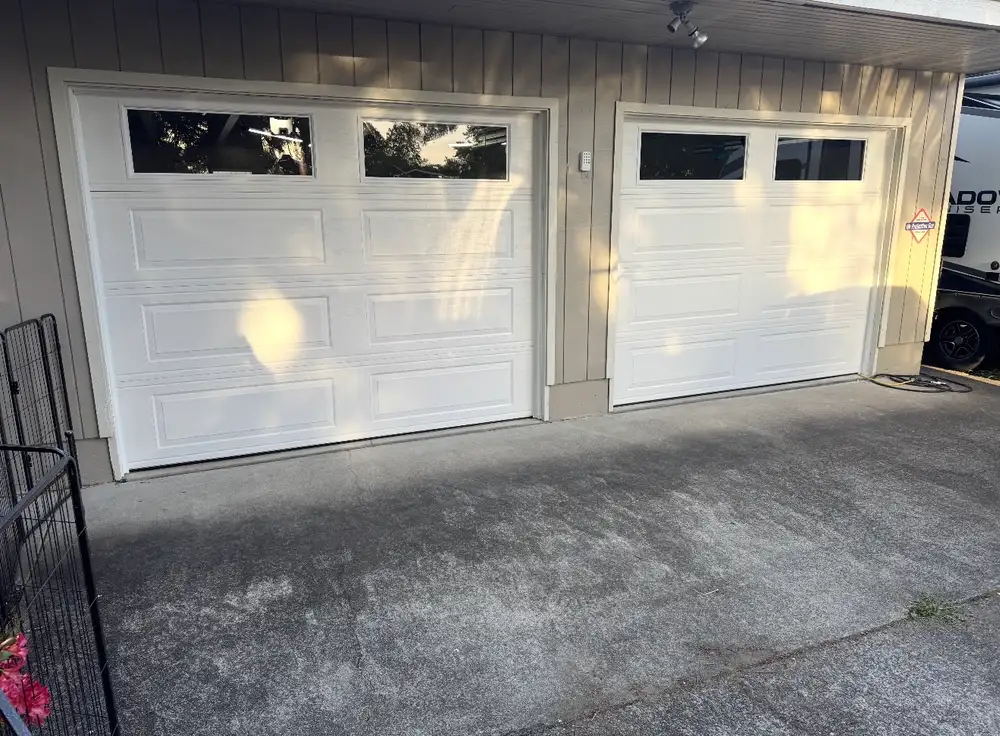 The same two openings fitted with new white raised-panel garage doors with window inserts